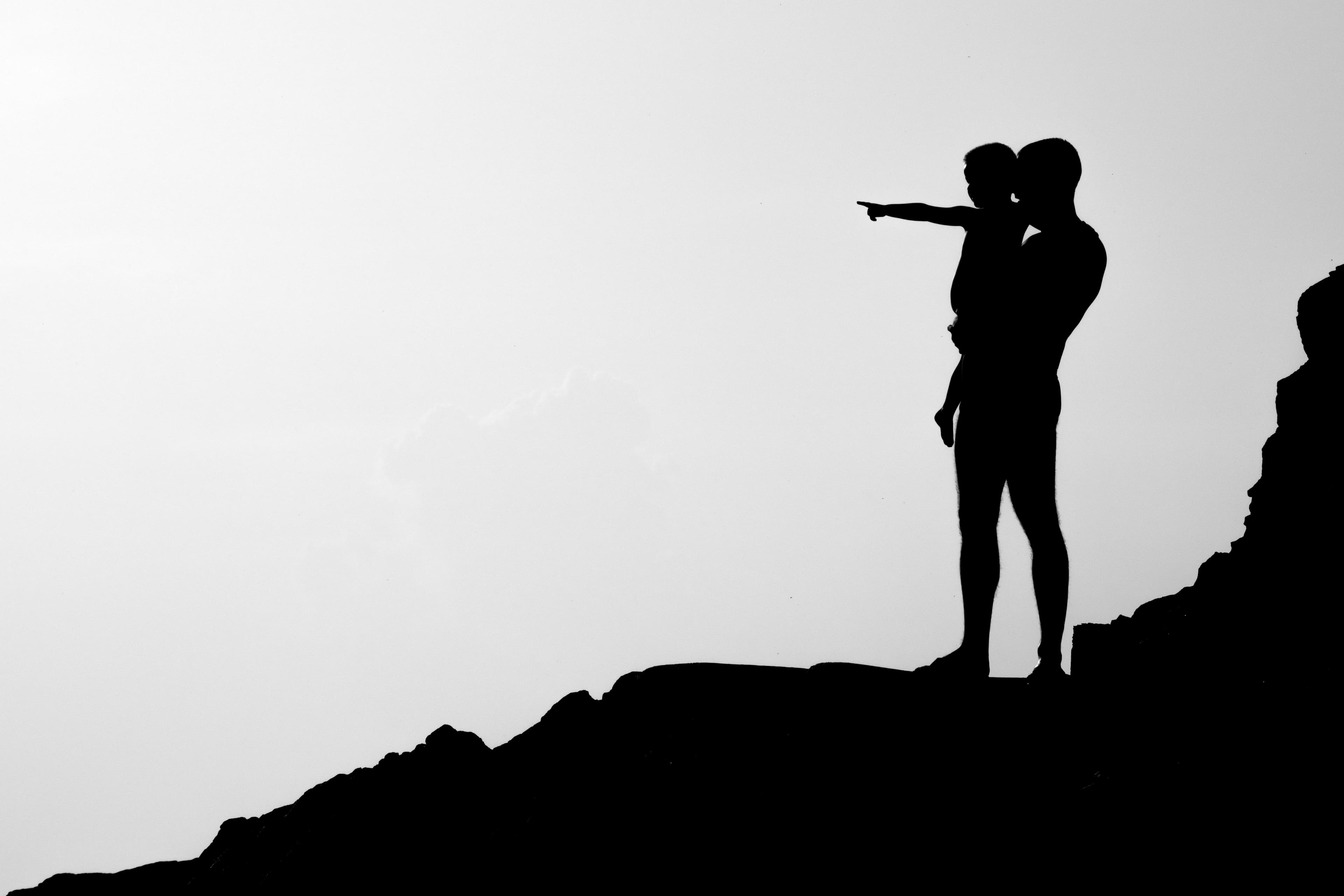 Child pointing into the distance being held by an older man in black and white in a mountain environment